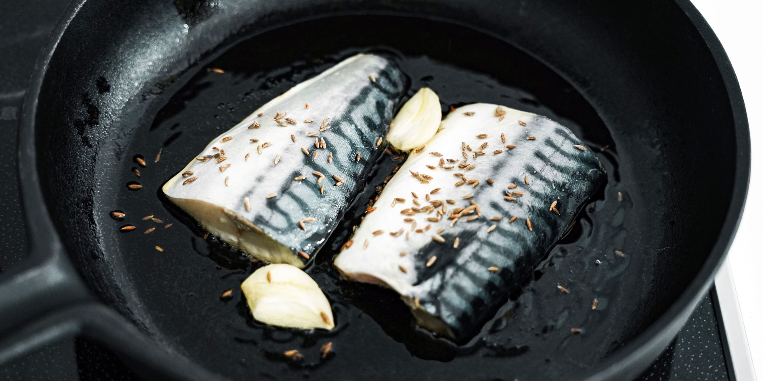 オリーブオイルとにんにくを弱火で加熱し、鯖とクミンシードを入れる